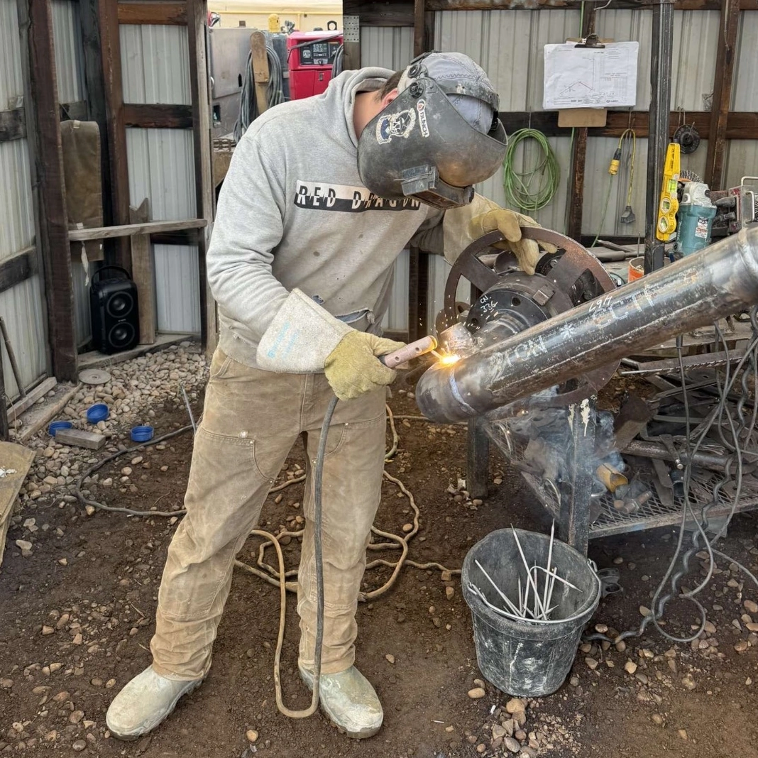 Skilled welder actively welding a steel pipe with full safety gear in a worksite environment